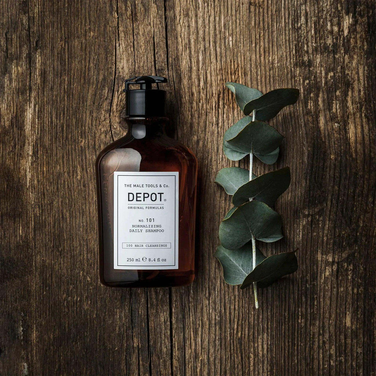 Depot No. 101 Normalizing Daily Shampoo bottle on wooden surface with eucalyptus branch.
